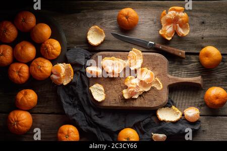 Reife runde Tangerinen und zur Hälfte auf einem alten Vintage Schneidebrett schneiden. Gesunde vegetarische Nahrung. Zitrusfrüchte, Ansicht von oben Stockfoto