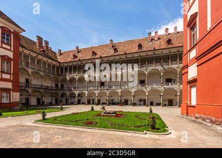 Opocno / Tschechische Republik - Juni 16 2020: Blick auf den Schlosshof mit Arkaden und roter Fassade. Grüner Rasen mit Statue und Blumen im Vordergrund. Stockfoto