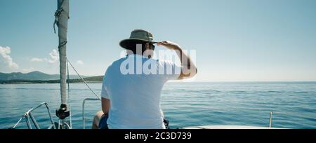 Mann, der auf den Schiffen sitzt, beugt sich und genießt die Jachtreise. Segel-, Segelsport- und Reisekonzept. Stockfoto