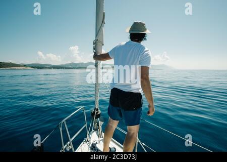 Mann, der auf den Schiffen steht, beugt sich und genießt die Jachtreise. Segel-, Segelsport- und Reisekonzept. Stockfoto