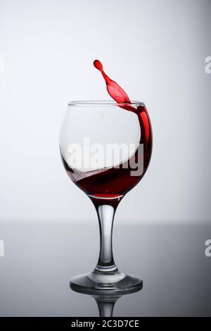 Spritzer Rotwein in einem Glas auf einem schwarzen glänzendem Glas auf weißem Hintergrund Stockfoto