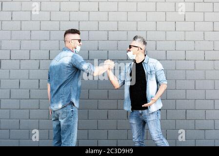 Zwei Freunde, die nach dem Ausbruch des Coronavirus mit Handschlag grüßen - Männer mit abgesenkten Schutzmasken - zwei Freunde, die soziale d nicht mehr respektieren Stockfoto