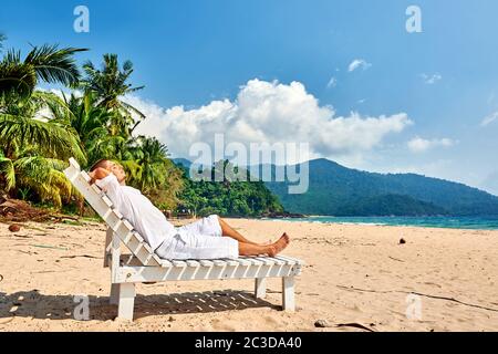 Mann in Weiß, der sich in der Sonnenliege am Strand entspannt Stockfoto