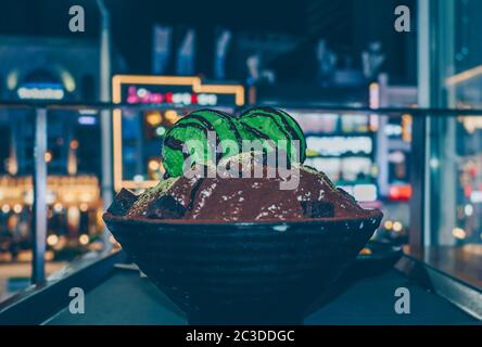 Frisch zubereiteter grüner Tee und Schokolade Bingsu mit Nachtstadt im Hintergrund Stockfoto