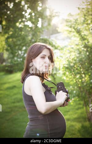 Schwangere Frau mit Fotokamera im Park stehend Stockfoto