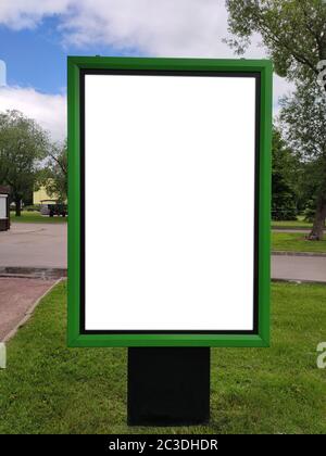 Ein grüner Infostand mit Platz für Text steht auf einer grünen Wiese in einem Sommerpark, vor einem Hintergrund von blauem Himmel und Bäumen. Modell. Vertikal. Stockfoto