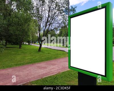 Ein grüner Infostand mit weißem Textplatz steht auf einer grünen Wiese in einem Sommerpark vor blauem Himmel und Bäumen. Modell. Hori Stockfoto