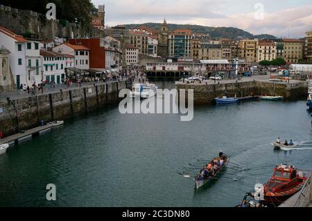 Ein Trainera Ruderboot, das den Hafen von San Sebastian, auch Fischerhafen genannt, mit Stadtbild von San Sebastian im Hintergrund betritt.San Sebastian.Gipuzkoa.Baskenland.Spanien Stockfoto