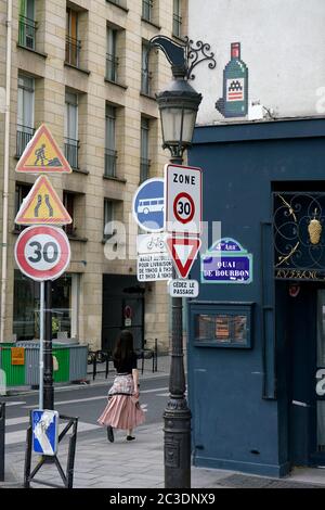 Eine Frau, die an einer Pariser Straßenecke in 4. Läuft Arrondissement mit Warnschildern für Verkehrs- und Geschwindigkeitsbegrenzungen im Vordergrund.Paris.Frankreich Stockfoto