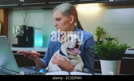Kaukasische Frau macht Selfie mit einem kleinen Hund, während am Computer in der Küche im modernen Zuhause sitzen. Stockfoto
