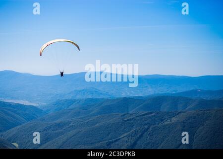 Paraglide Silhouette fliegen über Berggipfel, schöne Lichtstrahlen in hohen Bergtal auf Hintergrund Stockfoto