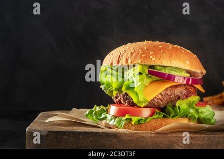 Burger mit Rindfleisch, Käse, Zwiebel, Tomaten und grünem Salat, ein Seitenblick auf dunklem Hintergrund mit Kopierraum Stockfoto