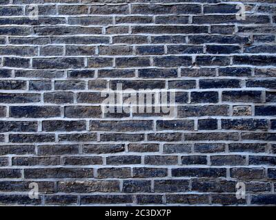 Eine alte Mauer aus schwarzen Steinziegeln mit grauem Zement Stockfoto