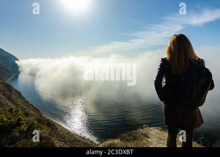 Das Mädchen beobachtet vom Berg aus eine ungewöhnliche Meeresdecke mit Wolken über dem Meer Stockfoto