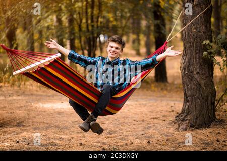 Mann in blauem Hemd und Hände oben Entspannen Sie in der Hängematte im Herbstwald Stockfoto