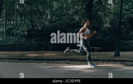 Bewegtes Foto eines jungen Sportlers Mädchen läuft im Sommer Nachmittag auf einem Trail. Frau, die körperliches Training macht. Stockfoto