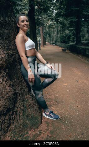 Athlet Frau genießen Tag in der Natur, die sich an einem Baum lehnt. Stockfoto