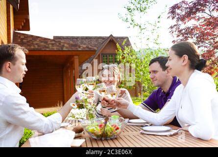 Glückliche Freunde, die mit Gläsern beim Abendessen am Tisch im Garten klimmten Stockfoto