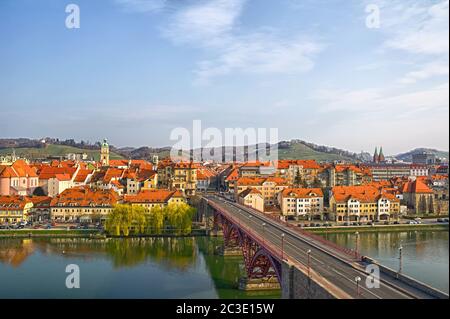 Maribor, Slowenien, Europa. Hauptbrücke (Glavni most, Stari most) über die Drau. Beliebte Flussufer Fastenzeit im Hintergrund. Stockfoto
