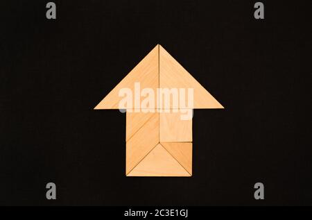 Flachlegen - Piktogramm, Symbol, Ikone des Hauses und Pfeil aus Holztangrammstücken. Einfarbiger Hintergrund aus dunkler Stoffstruktur. Stockfoto