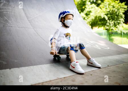 Ein Junge mit einem Skate in einer Maske, lernen zu skaten, in voller Schutz in Quarantäne. Stockfoto