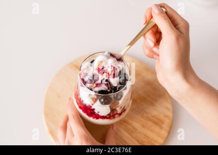 Hand des Mädchens mit Teelöffel frische appetitlich hausgemachten Joghurt über Glas mit gemischten Zutaten beim Frühstück am Morgen Stockfoto