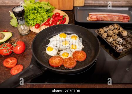 Mehrere gebratene Wachteleier und Tomatenscheiben, die mit gemahlenem schwarzem Pfeffer auf einer Pfanne mit frischem Gemüse umgeben sind Stockfoto