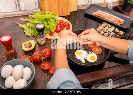 Hände von jungen Frau brechen frische Wachteleier auf heißen Pfanne während der Vorbereitung Frühstück durch Elektroherd in der Küche Stockfoto