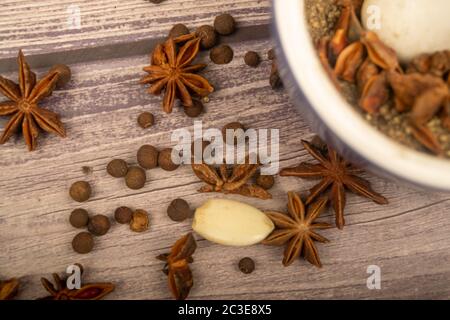 Piment in einem Keramikmörtel und verstreute Knoblauchzehen, Sternanis und Piment auf einem Holztisch. Nahaufnahme Stockfoto