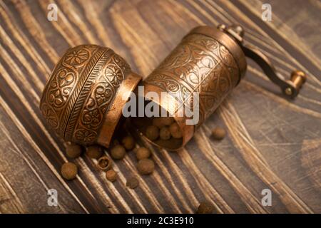 Eine offene manuelle Gewürzmühle und eine Streuung von gemahlenem Allspice auf einem Holztisch. Nahaufnahme Stockfoto