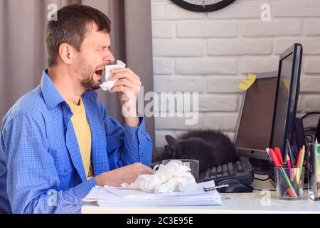 Der junge Mann niest sich an einem Computer Stockfoto