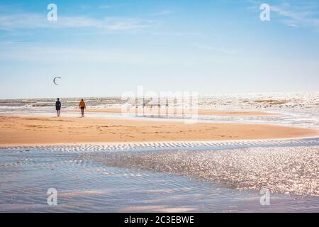 Zwei Personen gehen bei schönem Wetter auf den breiten Sandstrand Stockfoto