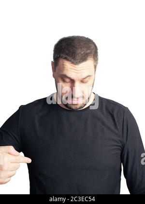 Ein bärtiger Mann in einem schwarzen Pullover schaut nach unten und zeigt mit dem Finger auf einen weißen Hintergrund Stockfoto