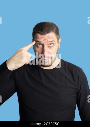 Ein unrasiert Mann mit braunen Augen in einem schwarzen Sweatshirt schaut auf und zeigt einen Finger mit Falten auf seine Stirn Stockfoto