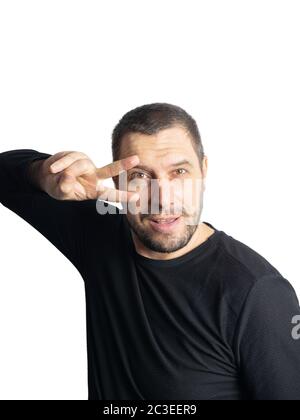 Ein Mann mit einem Bart in einer schwarzen Jacke hält zwei Finger in der Nähe seines Gesichts auf einem isolierten Hintergrund Stockfoto