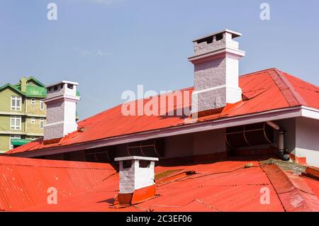 Kleine, weiß getünchte Kamine auf den roten, schrägen Blechdächern eines alten Kolonialzeithauses in der Bergstation von Shimla in Indien. Stockfoto