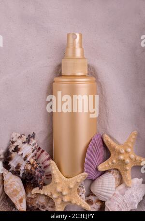 Sonnencreme-Flasche mit verschiedenen Muscheln und Seesternen vor dem sandigen Hintergrund. Stockfoto