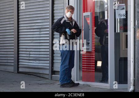 Ein Mann mit einer chirurgischen Gesichtsmaske benutzt während der Coronavirus-Sperrzeit einen Geldautomaten in Barry, Wales, Großbritannien. Stockfoto