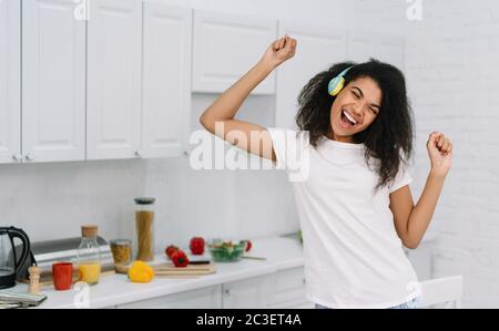 Glücklich emotionale Frau zu Hause tanzen, Spaß haben. Portrait der schönen afroamerikanischen Frau, die Musik mit kabellosen Kopfhörern hört Stockfoto