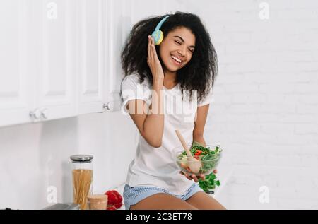 Happy emotional Mädchen hält Bawl mit frischem Salat, Musik zu Hause hören, lachen Stockfoto