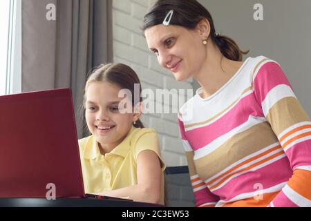 Glückliches Mädchen und Mädchen sitzen am Tisch und sehen sich den Laptop-Bildschirm an. Stockfoto