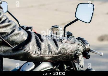 Die Hände eines Motorradfahrers in einem schwarzen Leder Jacke und Handschuhe auf dem Lenker eines Motorrads Stockfoto