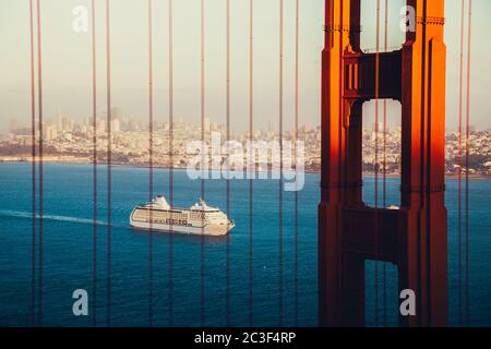 Wunderschöne Panoramasicht auf das Kreuzfahrtschiff, das sich der berühmten Golden Gate Bridge nähert, mit der Skyline von San Francisco im Hintergrund bei Sonnenuntergang, USA Stockfoto