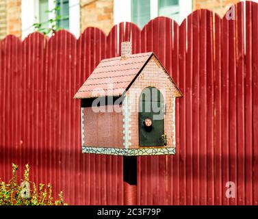 Mailbox in Form von einem kleinen Haus auf dem Hintergrund einer roten Zaun Stockfoto