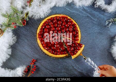 Womans Hand halten eine Schaufel mit Stück Kirschkuchen auf Weihnachten verzierten Tisch. Stockfoto