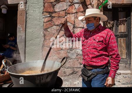 Real De Catorce, Mexiko. Juni 2020. Ein Arbeiter, der eine Gesichtsmaske als vorbeugende Maßnahme trägt, macht ein traditionelles mexikanisches Gericht aus Schweinefleisch vor einem Restaurant während der Wiedereröffnung von Unternehmen nach drei Monaten der Sperre aufgrund der Coronavirus-Pandemie. Kredit: Antonio Cascio/SOPA Images/ZUMA Wire/Alamy Live Nachrichten Stockfoto