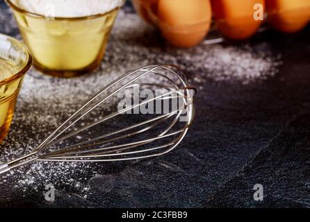 Kuchen Teig machen.Schneebesen, Mehl, Zucker und Eier auf schwarzem Hintergrund. Backkonzept. Stockfoto