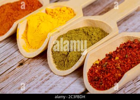 Vier verschiedene Gewürze in Holzlöffel. Paprikapulver, Curry, Senf und BBQ-Würze auf Holzgrund. Stockfoto