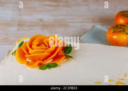 Karottenkuchen mit Frischkäse Zuckerguss bedeckt und mit einer Rose aus Persimmon geschnitten dekoriert. Stockfoto
