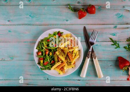Italienischer Nudelsalat mit frischem Erdbeer- und grünem Rucola-Salat auf rustikalem Holzhintergrund. Draufsicht Stockfoto